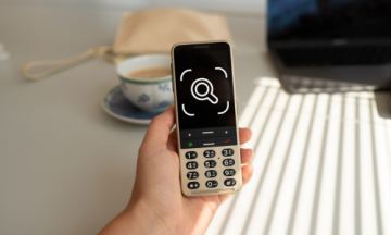 Eine Person, die ein BlindShell-Telefon in der Hand hält. Auf dem Display des Telefons wird ein Symbol für Observo