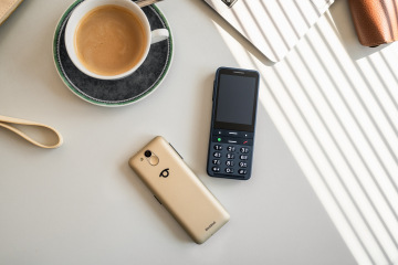 Die BlindShell Classic 3 in den Farben Sandgold und Ozeanblau liegen auf einem hellen Tisch neben einer Tasse Kaffee. Das Foto zeigt die Vorder- und Rückseite des Telefons mit einer großen Tastatur mit Reliefprägung, einfacher Bedienung und elegantem Design, das speziell für blinde und sehbehinderte Nutzer entwickelt wurde.