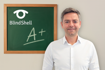 Jan Šimík, der Schulleiter von BlindShell, steht selbstbewusst in einem weißen Hemd neben einer Tafel, auf der das BlindShell-Logo und ein großes A+ zu sehen sind. Das Bild wirkt sehr motivierend, wie eine Anerkennung für Leistung und Führungsqualitäten.