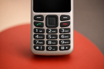 Nahaufnahme der Tastatur des BlindShell Classic Lite vor einem sanft unscharfen Hintergrund in warmen Beige-, Grau- und Rottönen. Das Bild hebt die großen, taktilen Zifferntasten hervor.