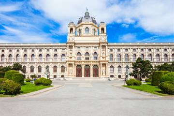 Die Vorderansicht des Kunsthistorischen Museums in Wien mit majestätischer Kuppel, aufwendigen Skulpturen und einer symmetrischen Fassade im Renaissancestil, umgeben von gepflegten Grünflächen.