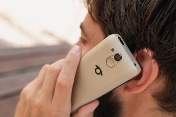 Ein Mann hält das BlindShell Classic 3 in der Farbe Sandgold während eines Telefonats ans Ohr. Das Foto zeigt die Rückseite des Telefons mit Kamera, SOS-Taste und dem BlindShell-Logo.